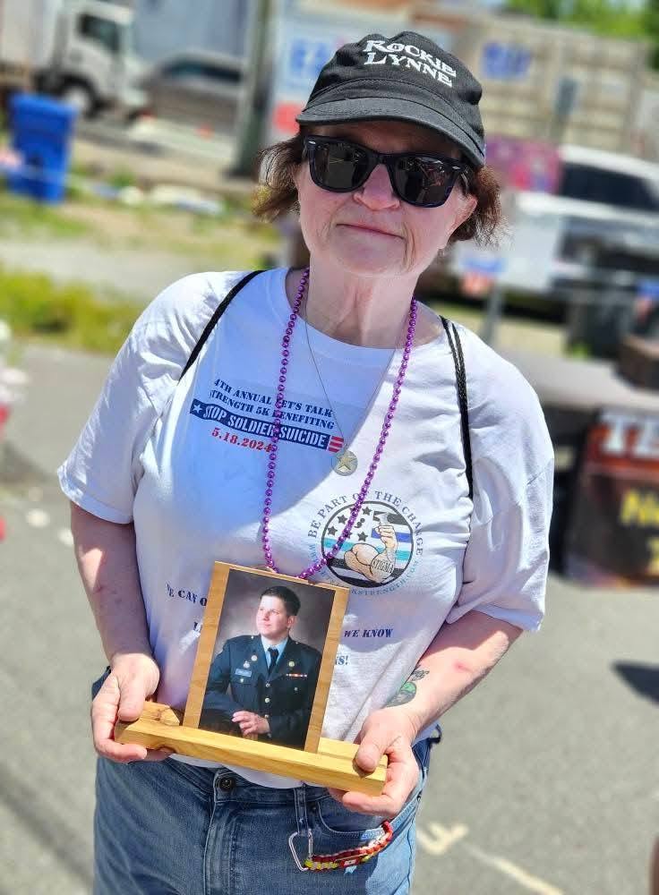 A woman holding a framed photo of a loved one lost to military suicide