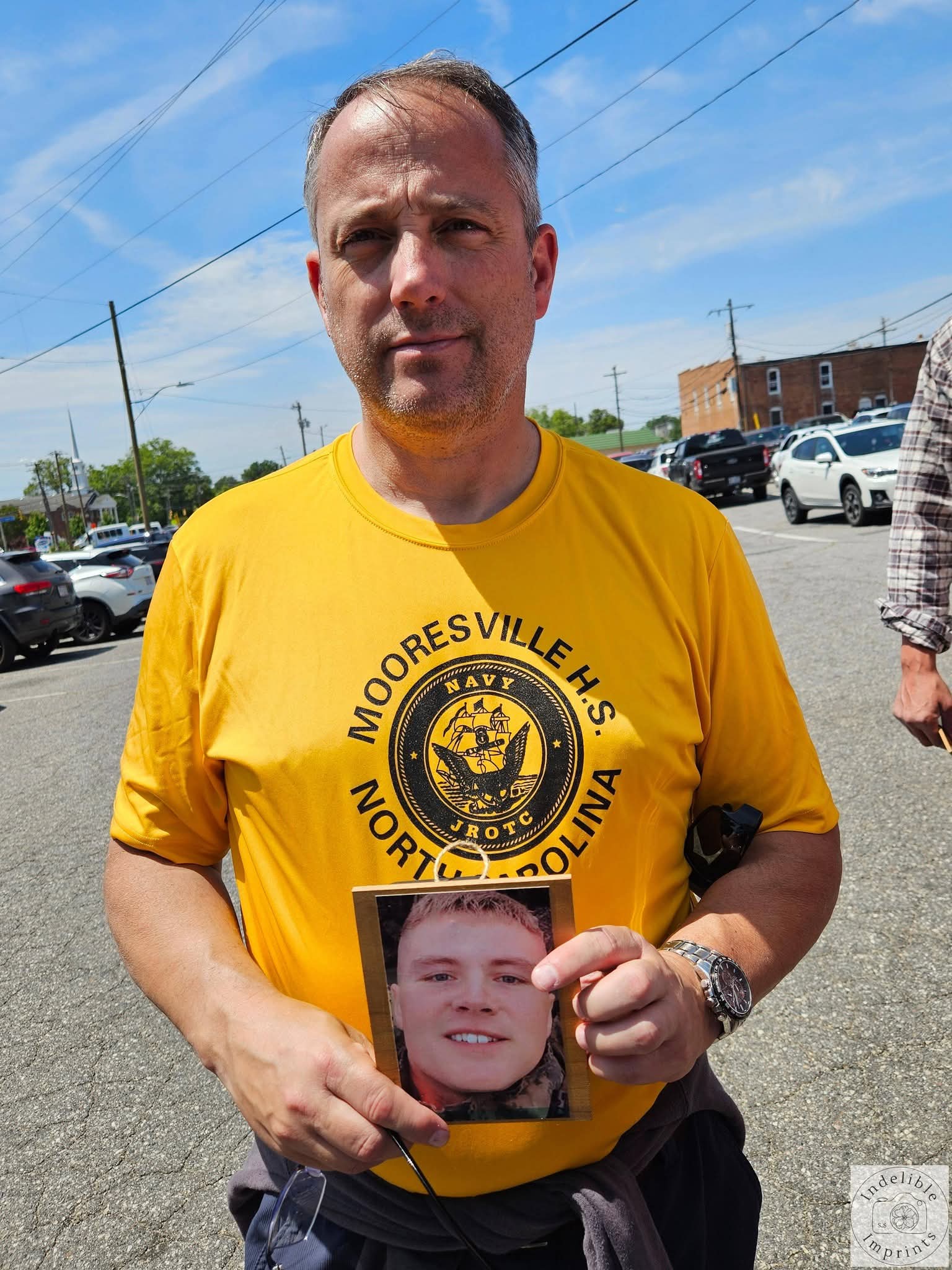 A supporter in a Mooresville H.S. Navy JROTC shirt holding a memorial photo