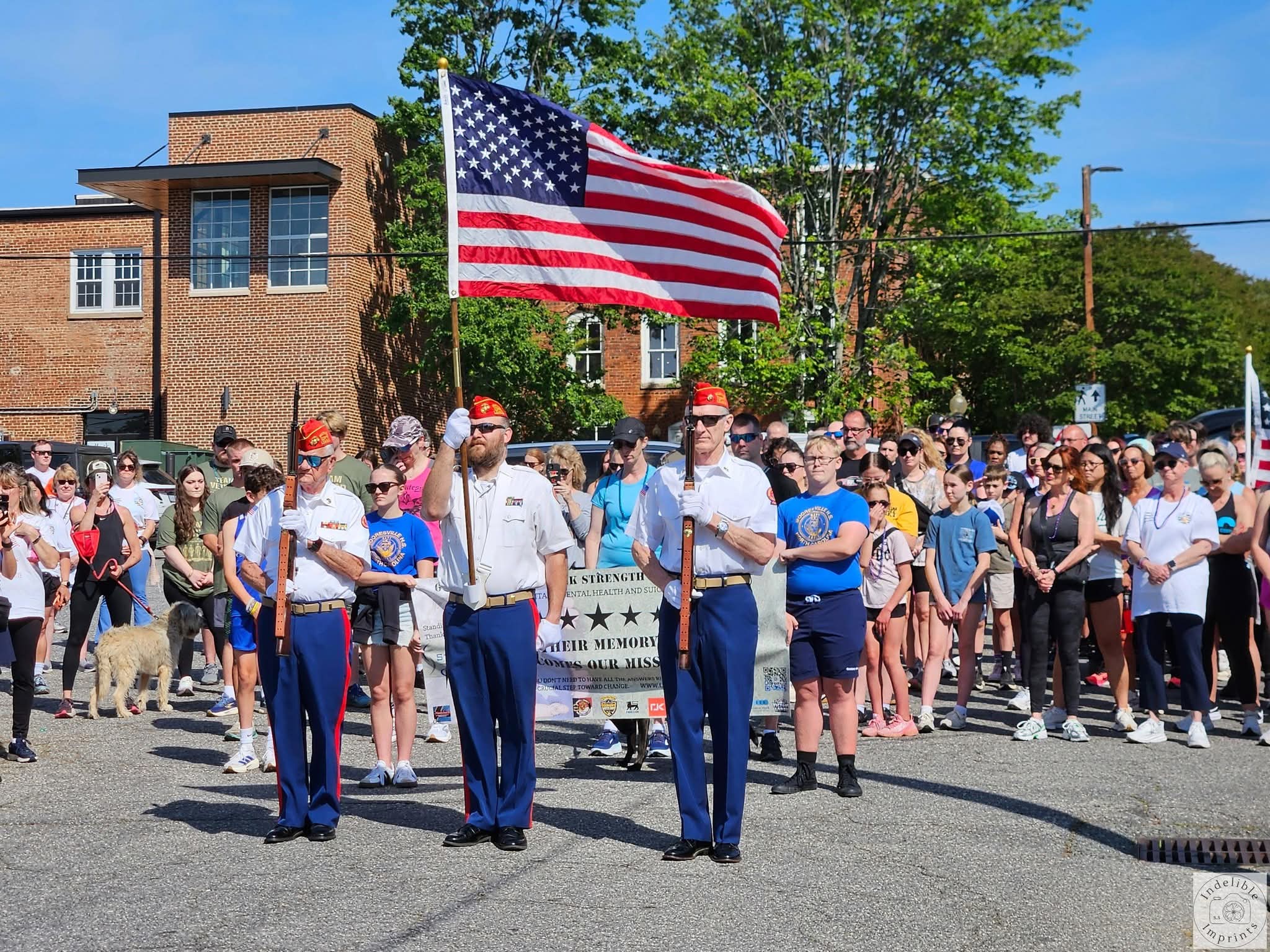 A color guard and a large crowd gathered behind a banner reading Their Memory Becomes Our Mission