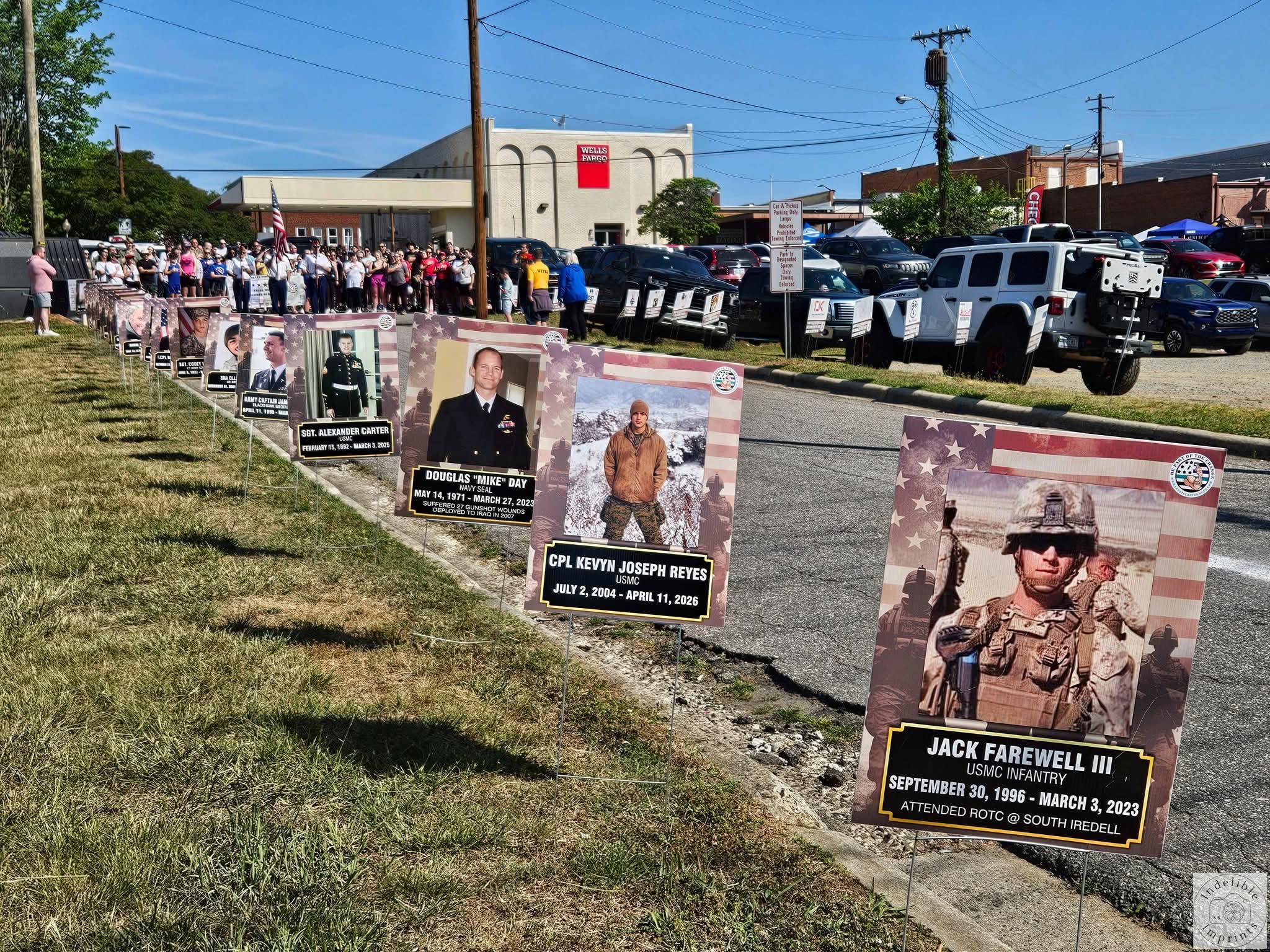 A row of memorial signs honoring fallen service members along the 5K route, with a crowd gathered behind