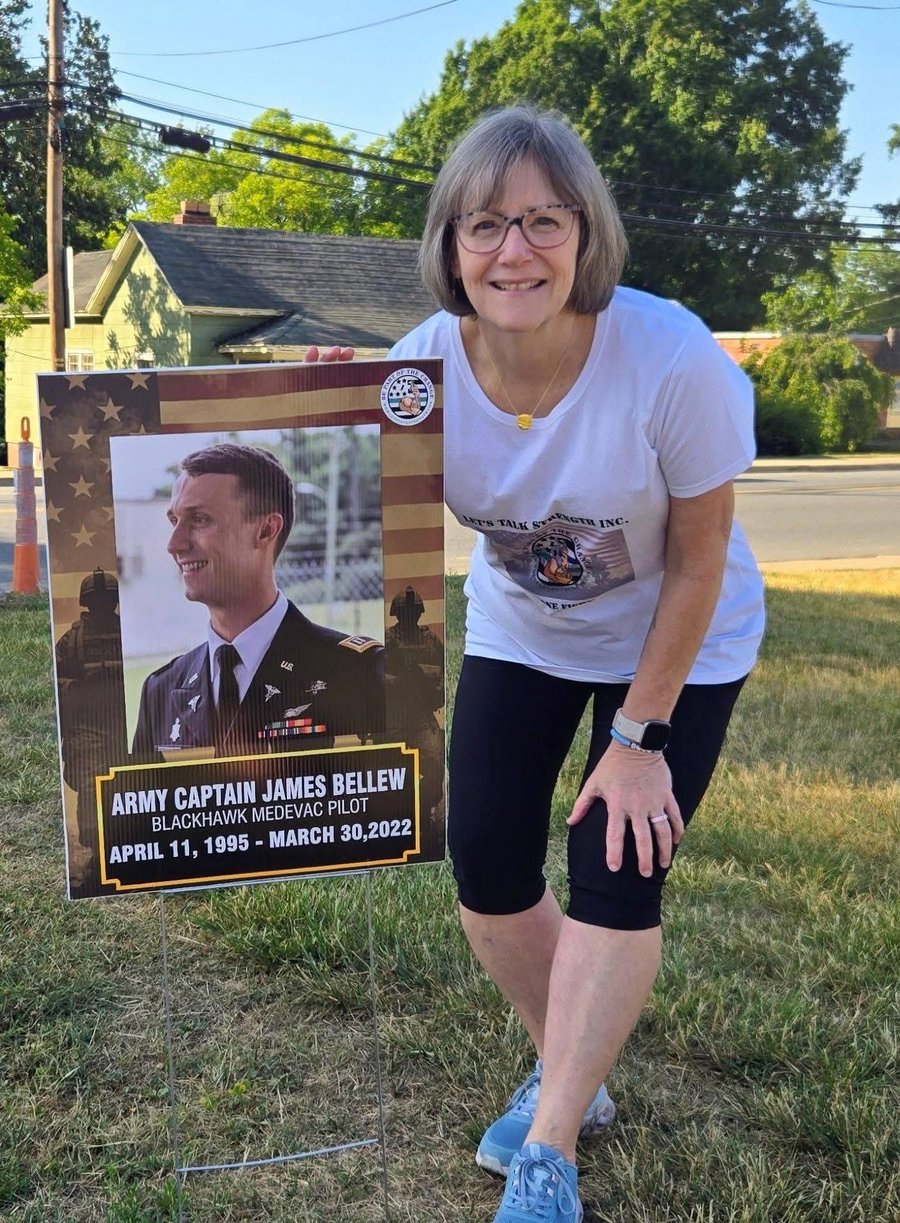 A woman standing beside a memorial yard sign honoring a fallen service member